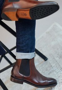 Bottines Chelsea en cuir marron avec une finition lisse, des panneaux latéraux élastiques et un talon empilé. Associées à un jean sombre avec des manches retroussées.