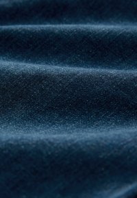 Țesătură din denim albastru închis care arată o textură netedă cu o strălucire subtilă, valuri pliate evidențiind adâncimea și greutatea materialului.