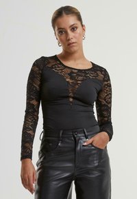 Zwarte bodysuit met lange mouwen, voorzien van een bovenlaag van kant met bloemenpatronen en een strak passend onderstuk. Gecombineerd met een hoge taille zwarte broek.