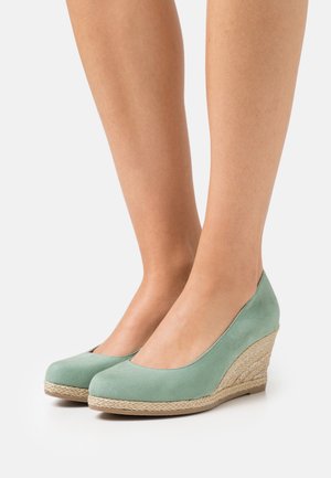 Zapatos de cuña de ante verde con punta redondeada, que cuentan con un tacón envuelto en yute y una textura suave. El diseño es bajo alrededor del tobillo.