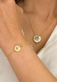Guldhalskæde og armbånd med cirkulære vedhæng, der har et trædesign mod en baggrund af perlemor, forbundet med fine kæder.
