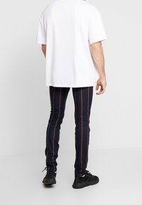 Navy striped leggings with orange vertical lines, made of stretchy fabric, paired with a loose white t-shirt and black sneakers.