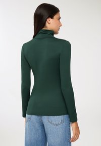 Zielony sweter z długim rękawem i kołnierzykiem, dopasowany krój, gładka tekstura, zestawiony z jasnoniebieskimi spodniami z wysokim stanem, widoczne detale szwów z tyłu.