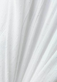Tessuto bianco con una superficie testurizzata caratterizzata da piccoli punti in rilievo. Il materiale è leggero, liscio e leggermente trasparente.