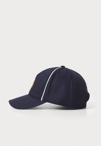 Tengerészeti baseball sapka ívelt karimával, fehér díszvarrással és logós részlettel az elülső részen. Texturált anyagból készült.