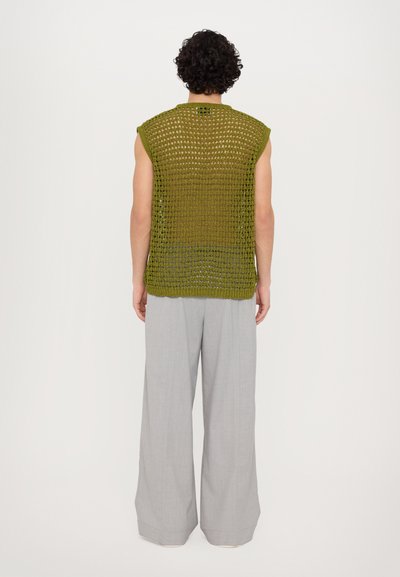 Olivgrünes gestricktes  ärmelloses Oberteil mit einem lockeren Häkelmuster. Kombiniert mit hellgrauen, weiten Hosen. Minimalistisches Design, lockere Passform.