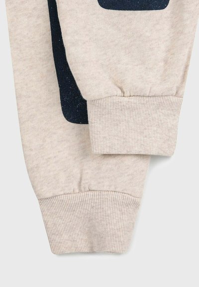 Helle beige Sweatshirtärmel mit ribbedem Bund, ausgestattet mit einem dunkelblauen geometrischen Muster. Weicher Stoff, lässiges Design mit kontrastierenden Farben.