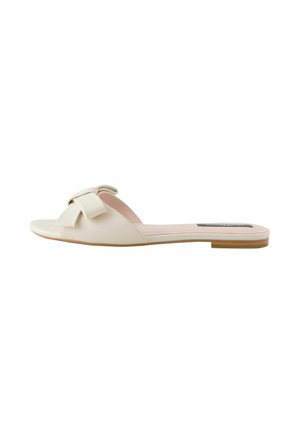 Sandalo piatto con fascia in faux leather color crema, caratterizzato da un ampio fiocco decorativo sulla cinghia e una suola in contrasto color cuoio.