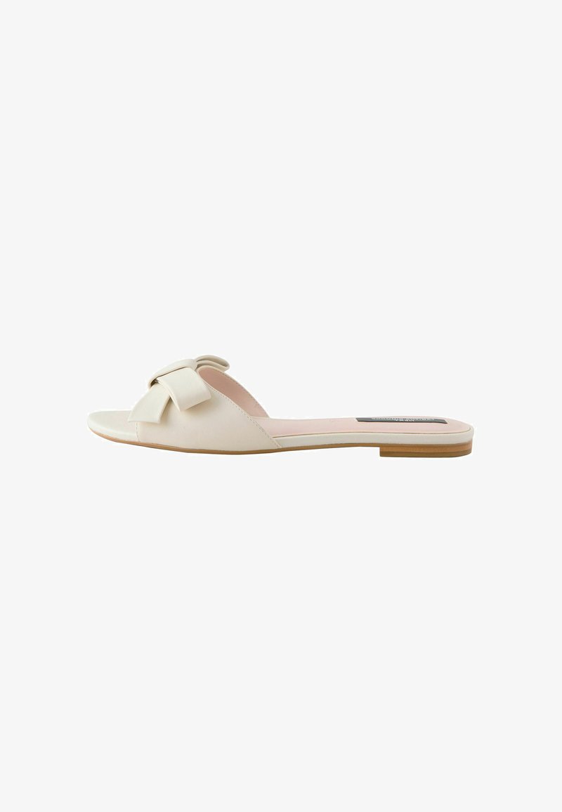 Flat slide sandal made of cream-colored faux leather, featuring a wide decorative bow on the strap and a contrast tan sole.