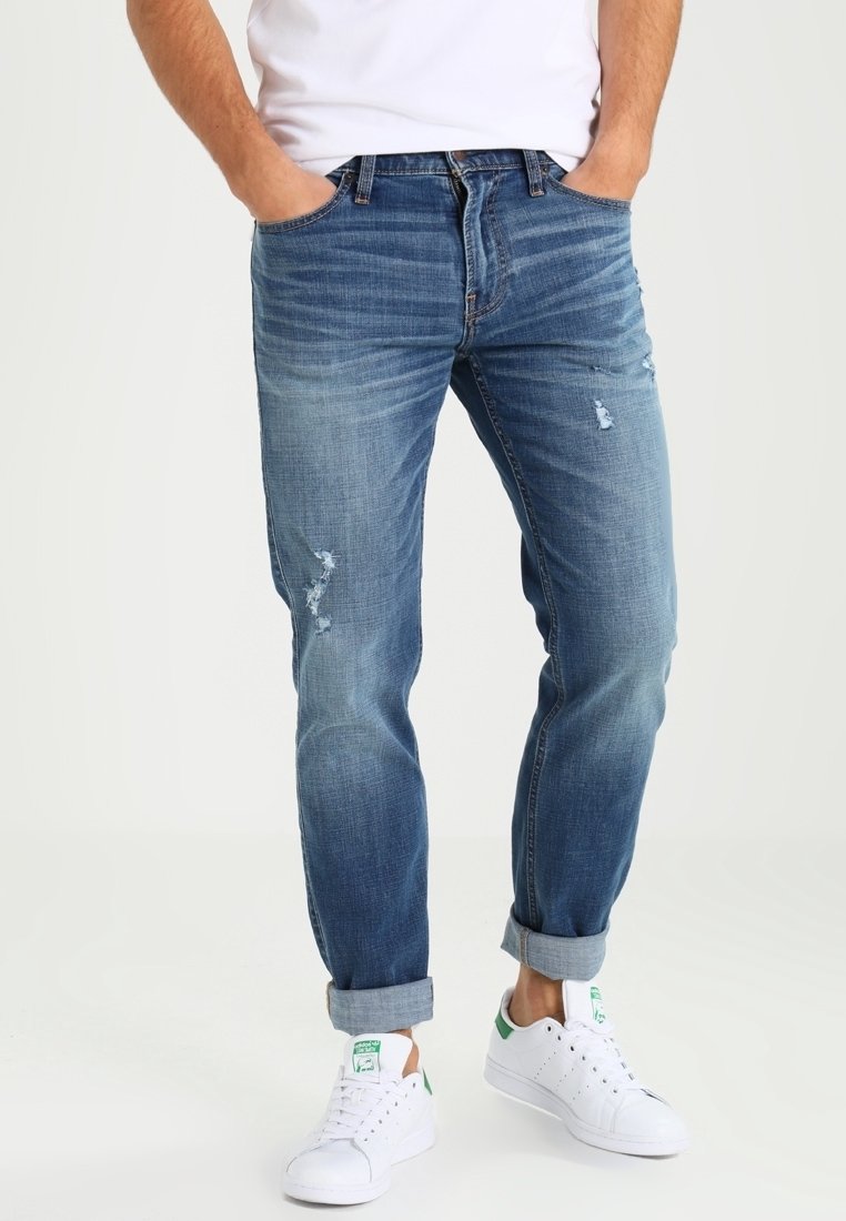 Ljust blå denimjeans med en avslappnad passform, massor av slitna detaljer, en urtvättad look och uppvikta avslut, kombinerat med vita sneakers.