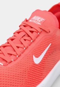 Punainen Nike-kengät, jossa on teksturoitu pinta, litteät nauhat ja valkoinen swoosh-logo. Suunnittelu on kevyt ja hengittävä materiaali.