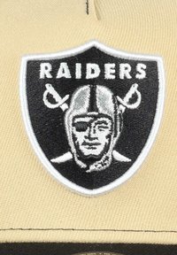 Schwarzes und weißes gesticktes Wappen mit einem Fußballspieler mit Augenbinde, gekreuzten Schwertern und dem Wort "RAIDERS" darüber.