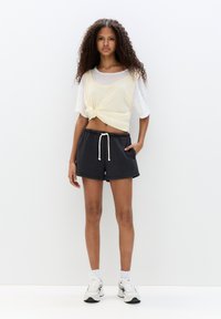 Light yellow knotted crop top paired with dark gray shorts featuring an elastic waistband and side pockets. Model wears white sneakers.