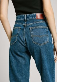 Jeans z denimu w średnim niebieskim kolorze o prostym kroju nogawki, z dwiema tylnymi kieszeniami, pomarańczowym przeszyciem i brązową skórzaną metką marki.
