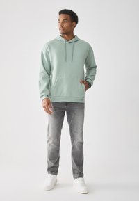 Mintgrønn hettegenser med snøring og frontlomme, kombinert med grå jeans og hvite joggesko, med en avslappet passform.