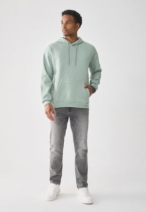 Mintgrønn hettegenser med snøring og frontlomme, kombinert med grå jeans og hvite joggesko, med en avslappet passform.