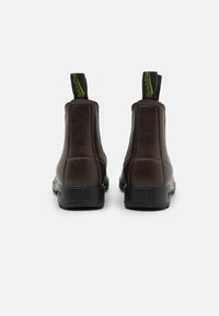 Bottines en cuir marron avec des panneaux élastiques sur les côtés et des semelles en caoutchouc. Talon noir et étiquette de marque contrastante verte à l'arrière.
