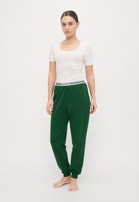 Hvit kortermet topp med firkantet halslinje, kombinert med grønne joggebukser med stripete elastisk midjebånd merket "Lacoste."