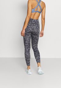 Leggings grigio mimetico con vita alta e reggiseno sportivo blu abbinato. I materiali sembrano leggeri e elasticizzati.