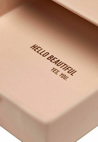 Rosa rektangulär låda med en slät yta som har präglad text: "HEJ VACKRA, JA DU." Insidan syns med en ren design.