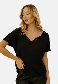 T-shirt noir à manches courtes, avec un décolleté en v orné de dentelle noire. Tissu doux avec une coupe décontractée, présentant une dentelle détaillée sur les épaules.