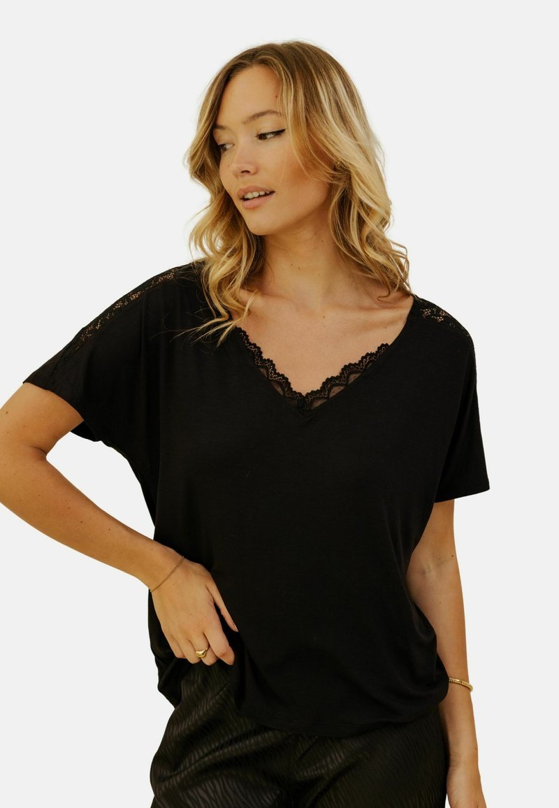 T-shirt noir à manches courtes, avec un décolleté en v orné de dentelle noire. Tissu doux avec une coupe décontractée, présentant une dentelle détaillée sur les épaules.