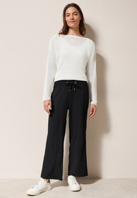 Suéter ligero de punto blanco de manga larga con escote barco; combinado con pantalones negros holgados de textura y zapatillas blancas.