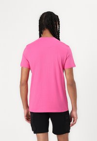 Camiseta de algodón rosa con mangas cortas, cuello redondo y costuras planas. Se lleva con pantalones cortos negros. Diseño simple sin patrones ni adornos distintivos.