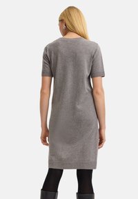 Graues Strickkleid mit kurzen Ärmeln, mittellangem Saum und gerippten Akzenten an den Bündchen und dem Saum. Getragen mit schwarzen Leggings und Stiefeln.