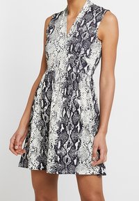 Sukienka z krótkim rękawem w czarno-biały wzór wężowej skóry, z dekoltem w kształcie litery V i rozkloszowanym dołem z teksturowanego materiału.
