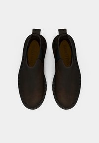 Chaussures marron à enfiler avec un dessus en cuir lisse, des panneaux élastiques sur les côtés et une semelle en caoutchouc texturée. Présente une marque à l'intérieur de la chaussure.