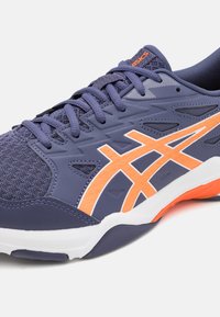Sports shoe in navy blue with orange accents. Features a textured upper, mesh panels, and a cushioned white sole. Contrast stitching visible.