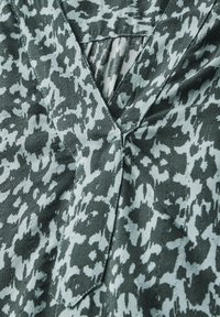 Camicia a maniche corte in un tessuto testurizzato con un motivo astratto verde e grigio chiaro, con scollatura a V e un lieve dettaglio di plissie.