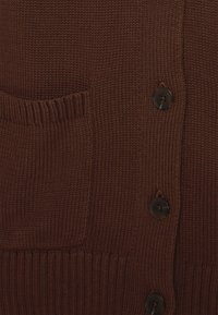 Hnědý pletený cardigan s výraznou kapsou, žebrovanými manžetami a pěti černými knoflíky vpředu. Hladká textura a střední tloušťka.