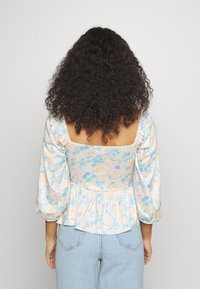 Top peplum floral com mangas bufantes, apresentando um decote quadrado, cores pastel suaves e um tecido estampado. Material texturizado e leve.