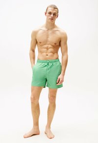 Bañador verde hecho de tejido ligero, con una cinturilla elástica con cordón y bolsillos laterales para mayor comodidad.