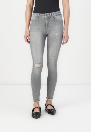 Gray distressed skinny jeans with frayed hem, featuring ripped accents and a classic five-pocket design, paired with black flat shoes.