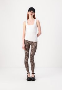 Fehér négyzetnyakú tank top, bézs és fekete leopárdmintás leggings, és fekete sapka. Fekete platform cipők bokapánttal.