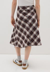 Falda de cuadros en tejido suave, con forma acampanada y una mezcla de patrones en burdeos, negro y gris; combinada con zapatillas blancas informales.