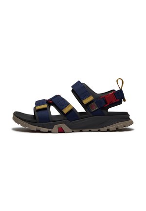 Sandalo outdoor da uomo con cinturini blu navy, suola nera, dettagli color cuoio e fibbia rossa, progettato per terreni accidentati e vestibilità regolabile.