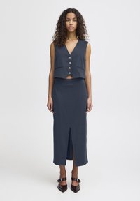 Námořnický dvoudílný outfit se skládá z krátké vesty s knoflíky a sukýnky s vysokým pasem a předním rozparkem, doplněný o lodičky s špičatou špičkou.