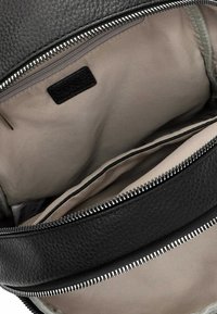 Interior de bolso de cuero negro con un forro beige suave. Cuenta con un zipper plateado y múltiples compartimentos para un almacenamiento organizado.
