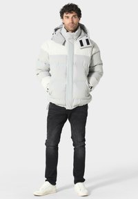 Vuorellinen harmaa-valkoinen takki korkealla kauluksella, säädettävällä hupulla ja kontrastivärisin mustin yksityiskohdin. Slim-fit-mustat farkut ja valkoiset tennarit.