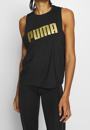 Osoba ubrana w czarny bezrękawnik Puma z złotym logo i czarne legginsy z białym przeszyciem, stojąca na jednolitym tle.