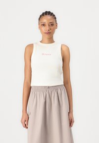 Débardeur blanc à côtes avec un logo "roxy" rose, associé à une jupe midi fluide de couleur brun clair avec une taille élastique.