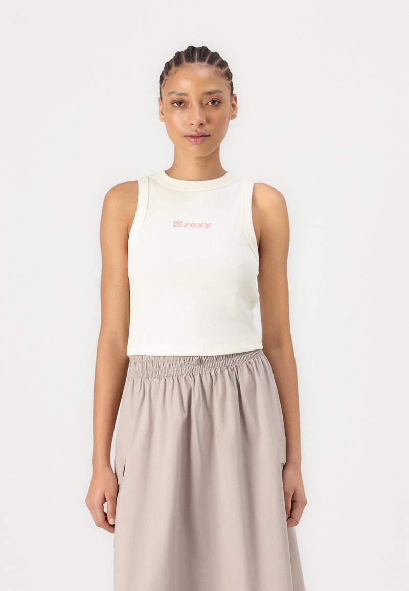Débardeur blanc à côtes avec un logo "roxy" rose, associé à une jupe midi fluide de couleur brun clair avec une taille élastique.