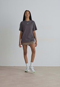 Siva Nike majica s okruglim izrezom i kratkim rukavima, u paru s bež suknjom. Model nosi bijele tenisice s zelenim detaljima.