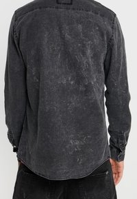Camicia di jeans nera con una texture sbiadita, maniche lunghe, polsini con bottoni e orlo curvo. Presenta un design con yoke sulla schiena.