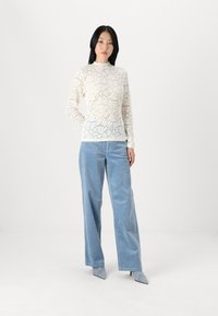 Top en dentelle à manches longues en ivoire avec des motifs floraux, associé à un pantalon large en velours côtelé bleu clair et des talons à bout pointu. Design texturé simple.