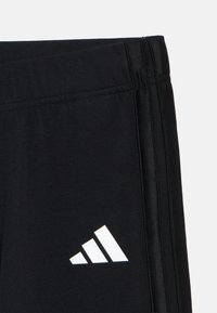 Μαύρα αθλητικά σορτς με υφή στο ύφασμα, πλαϊνές ρίγες και λευκό ανάποδο τρίγωνο λογότυπο στην κάτω αριστερή πλευρά.